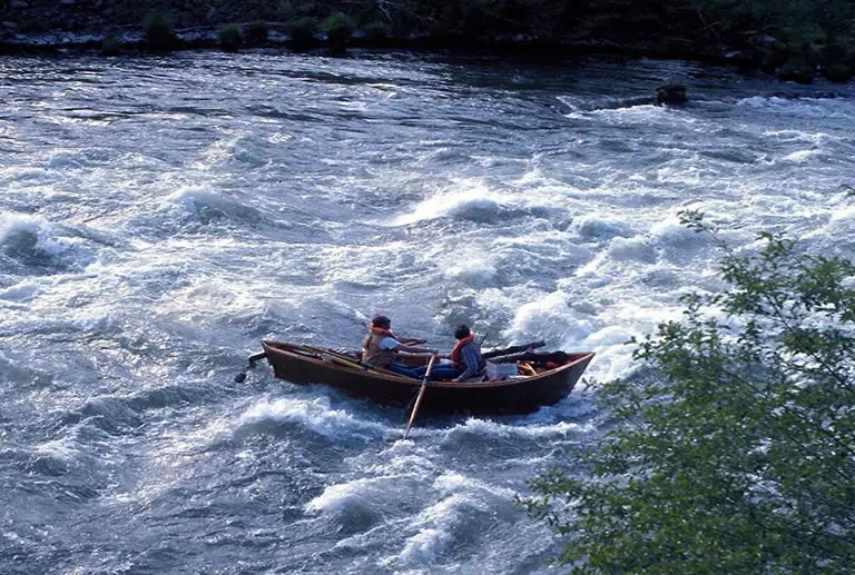 Two people using a drift boat in whitewater
